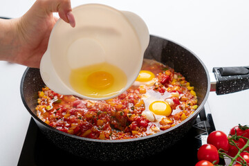 The cook puts the fourth egg in the Pan with  Bell Peppers, Tomatoes  are fried on the Stove. Recipe cooking process for Shakshuka and Menemen. Step by step. Fifteenth photo.
