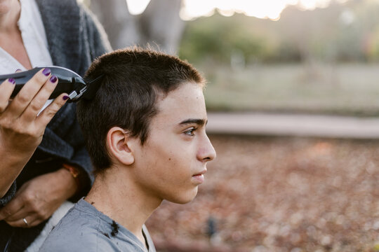 Happy teenager boy shaving hair outside home