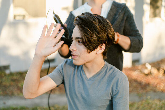 Happy teenager boy shaving hair outside property