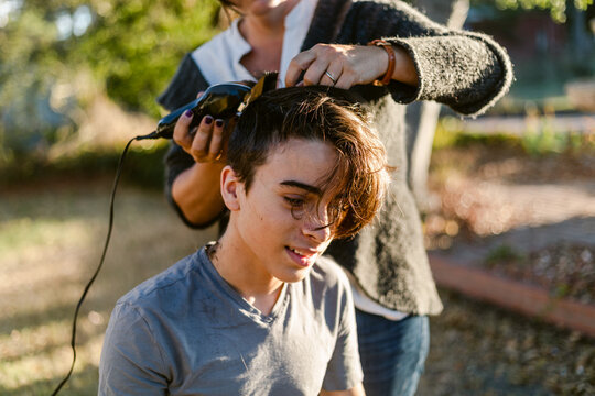 Teen boy getting buzz haircut By mother outdoors