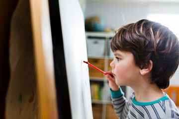 Boy concentrates while painting on easel