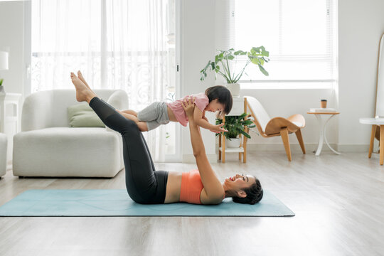 Happy young mother lying on yoga mat, lifting in air joyful