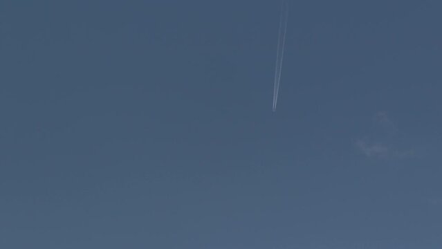 A jet plane flies high in the sky leaving a white trail behind it