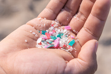 Micro plastics or Microplastics found on the beach on a person's hand on Mexico, sea sand in the background.