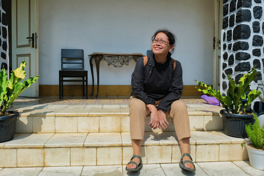 A middle-aged woman sitting on the steps of a terrace with a backpack on her back