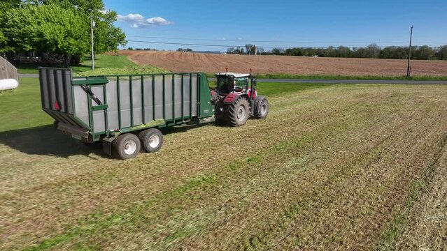 Wide lens aerial tracking shot of Massey Ferguson tractor pulling full silage trailer.