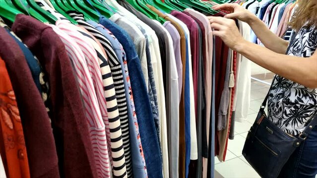 Woman shopping for clothes in a clothing store. Lined up colorful pieces of clothes being selected by customer.