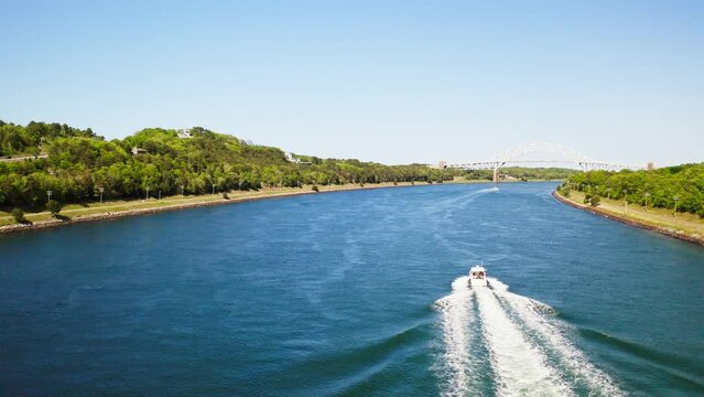 Drone follows a boat on Cape Cod Canal with Sagamore Bridge in the distance.