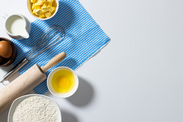 Directly above shot of flour, butter, milk, egg, yolk in bowls with whisk, rolling pin and napkin