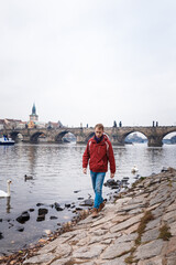 male tourist in red jacket, blue jeans on embankment of Prague