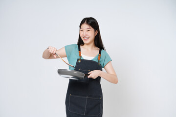 Naklejka premium Young woman wearing kitchen apron cooking and holding pan and spatula isolated on white background.