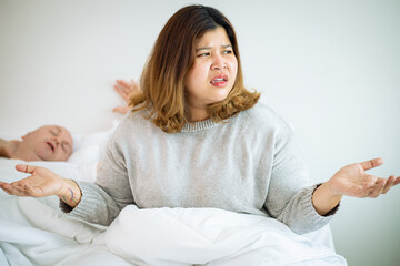 Woman suffers from her male partner snoring while lying in bed together. Snoring is one of the factors of sleep deprivation. 