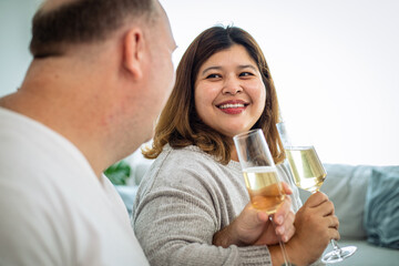 Happy senior couple in love hugging, laughing, drinking wine, enjoying talking, having fun together celebrating Valentines day dining at home