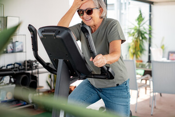 Fototapeta na wymiar People sport concept. Smiling senior woman cycling doing exercises to stay fit. Elderly woman riding stationary bicycle in the home terrace