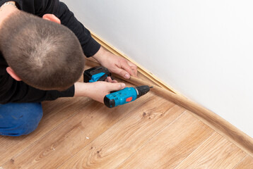A worker installs a skirting board on the floor in a room