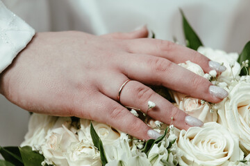 Obraz na płótnie Canvas Bride's hand with a wedding ring on a bouquet of white roses