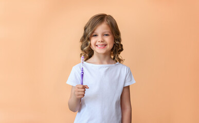 The child is holding a toothbrush and is going to brush his teeth against a beige background. Children's dentistry. Healthy baby milk teeth and gums. copy space