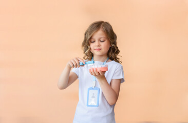 A little dentist girl holds a model of a human jaw and a toothbrush in her hands to demonstrate proper tooth brushing isolated on pink studio background. International Dentist's Day. copy space