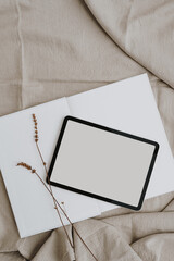 Tablet pad screen with empty free copy space for mock up, dried grass on neutral beige linen cloth. Bright aesthetic social media branding, online shopping template with neutral beige colour