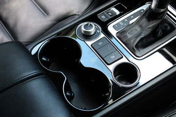Car inside, cup holders and armrest, black leather seats, automatic transmission close up. ...