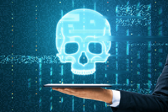 Close up of male hand holding tablet with glowing digital blue glitch skull hologram on dark background. Virus, crime and hacking concept.