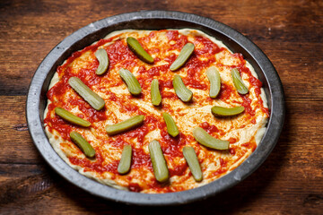 cooking pizza with pickled cucumbers. Dough smeared with tomato sauce.