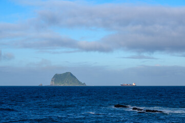 Rapidly changing clouds over an island in the sea. View of Keelung Island from Wanli Beach in New Taipei City. Taiwan.