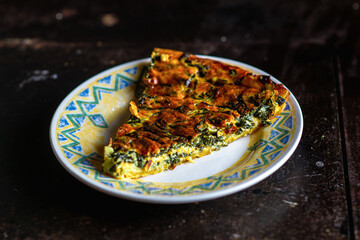 Piece of freshly made spinach and cheese pie on a plate on a dark background. Vegan pie.