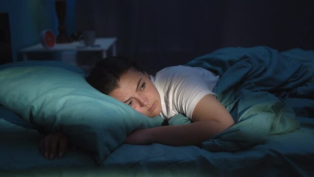 Young woman suffering from insomnia lies at home in bed unable to sleep in the middle of the night