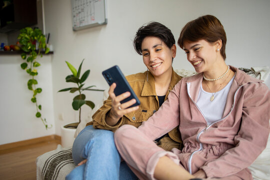 Same Sex Couple At Home Using Mobile Phone. Latin Lgbtq Couple Using Mobile Phone To Take A Selfie 