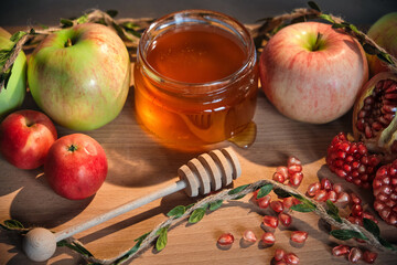 Traditional Jewish new year food. Happy Rosh Hashanah concept. Red and green apples, pomegranate and seeds and honey in a glass jar on wooden background.
