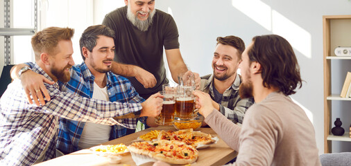 Group of happy men enjoying free time, having a party at home, sitting at a table, drinking beer, clinking mugs, eating pizza, and having fun together. Banner background. Friends' party concept