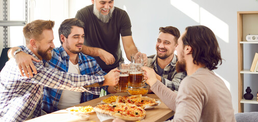 Group of happy men enjoying free time, having a party at home, sitting at a table, drinking beer, clinking mugs, eating pizza, and having fun together. Banner background. Friends' party concept