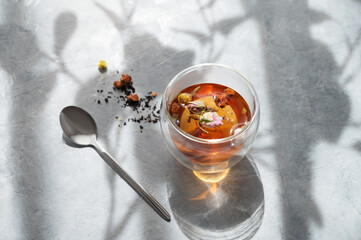 A  glass of tea with herbal and flowers and spoon on a light background with a shadow. Healthy...
