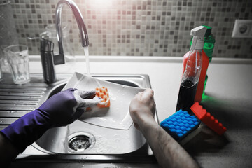 A white bottle with dishwashing gel on the background of a sink with dirty dishes and pouring water from a tap.