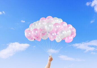 Boy hand with colorful balloons on bright sky background.