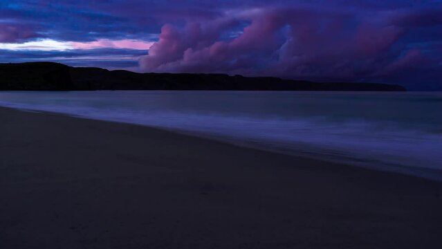 Time lapse of the sunsetting over a sandy beach as the tide comes in. Clouds roll in the wind in the distance over the cliffs. Filmed on the Isle of Lewis, part of the Outer Hebrides of Scotland.