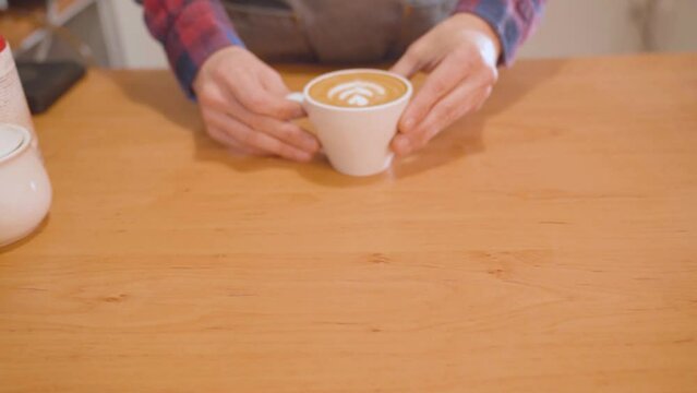 Barista puts down to counter cup of coffee with latte art. Customer grabs it