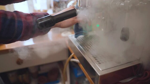 Barista cleans steam wand of coffee machine with cloth and steam. Closeup