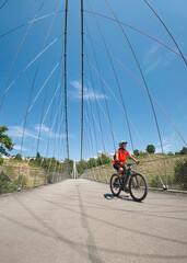 attractive senior woman crossing river Neckar with her electric mountain bike near city of...