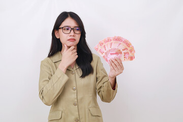 Thoughtful and confused young government employee standing while holding indonesian banknotes