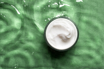 Jar of cosmetic cream on green water