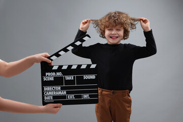 Happy cute boy performing while second assistant camera holding clapperboard on grey background....