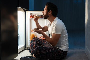 Man eating donuts near refrigerator in kitchen at night. Bad habit
