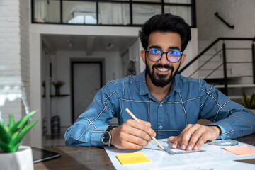 Dark-haired young man sitting at the table and preparing a project draft