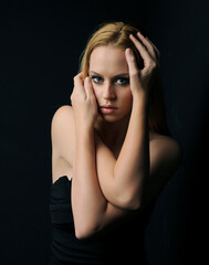 close up portrait of beautiful young blonde model with blonde hair, gestural arm poses, isolated  against a dark black studio background.