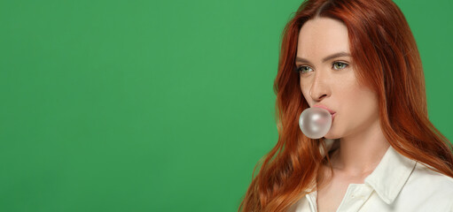 Beautiful woman blowing bubble gum on green background. Space for text