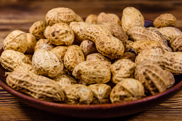 Ceramic plate with heap of unpeeled peanuts on wooden table