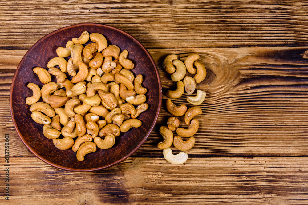 Wall mural Ceramic plate with roasted cashew nuts on a wooden table. Top view - Wall murals