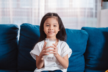 Cute Asian girl drinking milk at home to nutrition vitamin healthy and strong teeth.